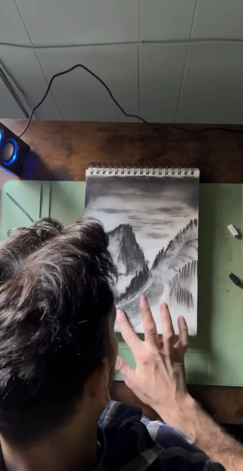Nadir drawing a charcoal mountain landscape in a sketchbook